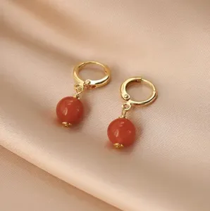 Detailaufnahme von goldenen Creolen mit eleganten roten Achatperlen auf Seidenhintergrund