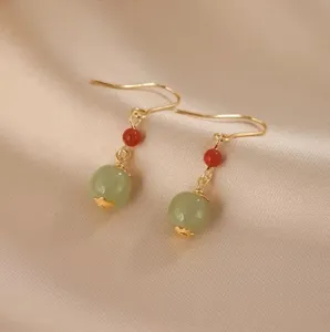 Detailansicht eleganter Goldohrringe mit rotem Achat und grünen Jadeperlen auf Seide.