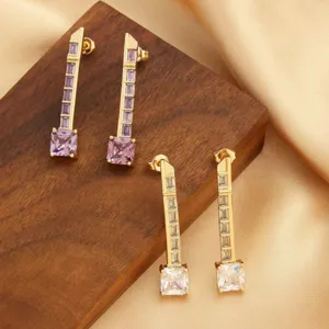 Elegante goldene Hängeohrringe mit lila und klarem Zirkon auf Holz - Detailansicht