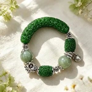 Nahaufnahme eines grünen geschnitzten Perlenarmbands mit floralen Silberelementen und Anhängern.