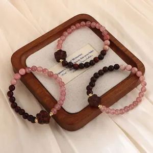 Detailaufnahme von Sandelholz- und Erdbeerquarz-Perlenarmbändern mit Holzblumenanhänger
