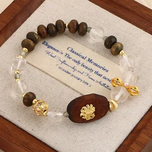 Natürliches Adlerholz- und Kristallperlenarmband mit goldenem Lotus-Anhänger auf Holztablett.