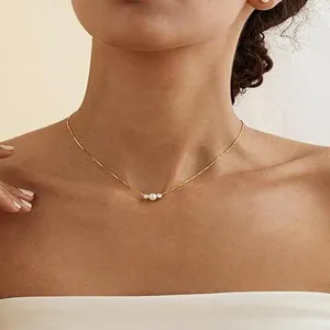 Nahaufnahme einer eleganten Goldkette mit drei kleinen Perlen an einem weiblichen Modell