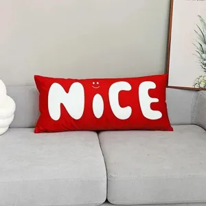 Detalle de cojín largo rojo, cojín decorativo con impresión de letras NICE en el sofá.
