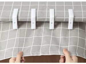 Vista ravvicinata di quattro clip in plastica bianca che fissano una tovaglia a scacchi