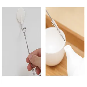 Détail d'une brosse longue et fine nettoyant un bec de théière et suspendue à un crochet.