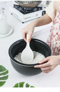 Detailansicht eines weißen, antihaftbeschichteten japanischen Reislöffels beim Schöpfen.