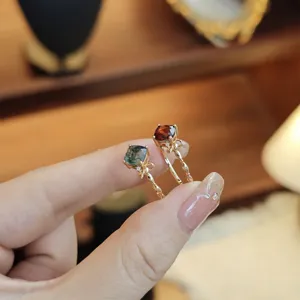 Close-up of hand holding natural moss agate and red stone S925 silver rings with bow detail
