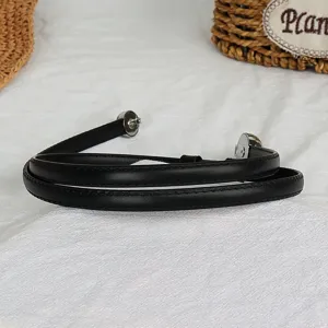 Detailed close-up of a black thin leather belt with silver metal double buckles on white fabric.
