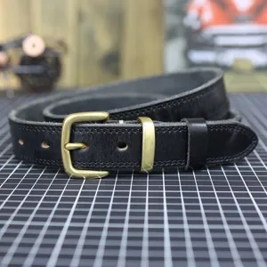 Close-up of black genuine leather belt with vintage brass buckle on professional craft grid mat