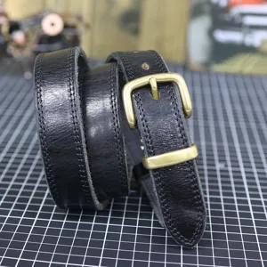 Detail shot of black genuine leather belt with retro brass buckle, showing fine stitching.