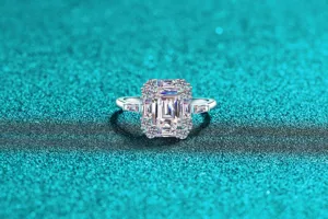 Detailed macro shot of an emerald-cut moissanite silver halo ring on teal glitter.