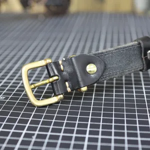 Close-up detail of genuine black leather belt featuring vintage brass buckle and stitching.