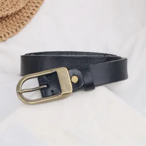 Black genuine leather belt detail with vintage brass pin buckle on white cloth background.