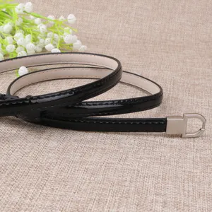 Détail de ceinture fine en cuir vernis noir avec boucle en métal argenté et belles finitions.