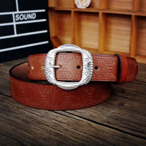 Vintage leather belt detail showing embossed pattern and intricate metal buckle on wooden table.