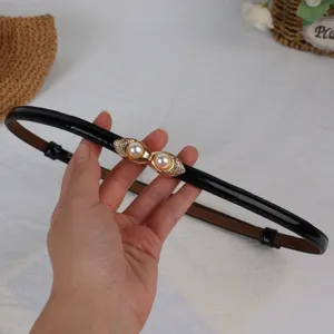 Detail shot of the black patent leather belt featuring elegant gold-tone double pearl buckles.