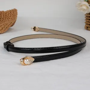 Close-up detail of the black patent leather thin belt featuring a pearl and gold metal buckle.