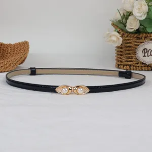 Closeup detail of a slim black patent leather belt featuring a delicate gold pearl eye clasp.