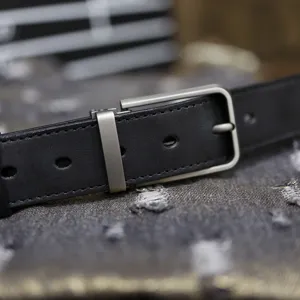 Leather belt detail shot showing black cowhide strap and matte metal pin buckle design.