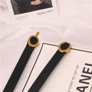 Detalle de primer plano de cinturón fino de cuero negro para mujer con hebilla ovalada dorada.