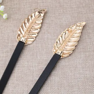 Detail close-up of thin black leather belt featuring elegant gold leaf shaped metal buckle.