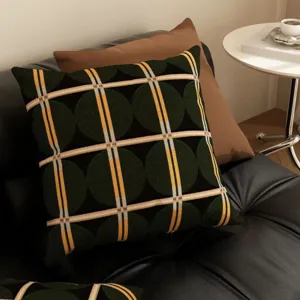 Gros plan sur un coussin rétro géométrique vert foncé sur un canapé en cuir moderne.