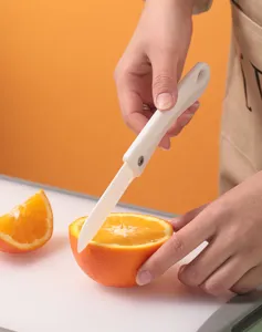 Gros plan d'un couteau pliant portable en céramique blanche coupant une orange fraîche.