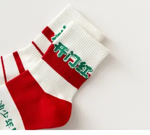 Red and white mid-tube socks detail, featuring green woven auspicious blessing text.