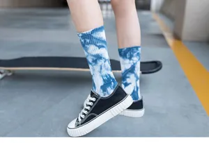 Detailed view of trendy blue tie-dye crew socks worn with black sneakers on skateboard background.