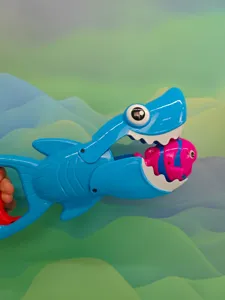 Close-up detail of blue shark grabber toy catching pink fish for kids water bath play.