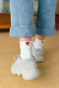 Detail shot of white cotton socks featuring a cute rainbow heart embroidery and rolled cuffs.