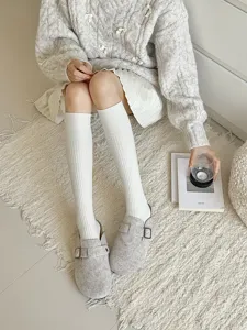 Detailopname van gezellige witte gebreide kniekousen gedragen in een comfortabele binnenomgeving.