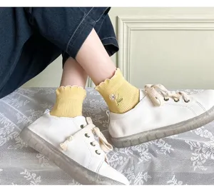 Detail shot of yellow ruffle trim socks with cute flower embroidery worn with white sneakers.