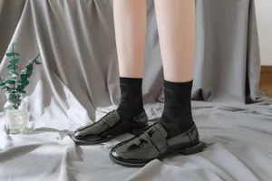 Detail shot of black sheer patterned mid-tube socks paired with patent leather loafers.
