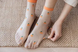 Vue détaillée de chaussettes transparentes en soie de verre avec broderie d'orange et poignets.