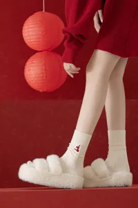 Detailed view of cream ribbed knit socks with a red snake embroidery paired with fluffy slippers.