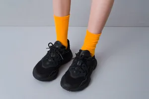 Close-up detail of bright yellow ribbed crew socks worn with black sneakers on grey.