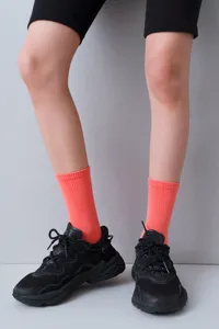 Close-up of coral pink ribbed mid-calf socks styled with black sneakers and shorts.