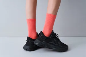 Detail shot of bright coral ribbed mid-calf socks worn with black sneakers, clean studio style.