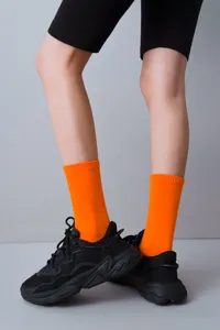 Detailed view of bright orange ribbed mid-calf socks styled with black chunky sneakers.