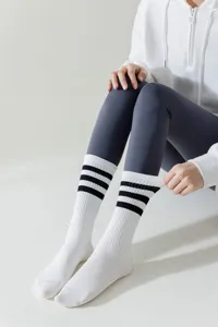 Detailed view of white athletic crew socks with three black stripes, worn with grey leggings.