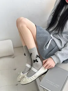 Close-up detail of grey mid-calf socks featuring cute black bows, soft knit fabric.