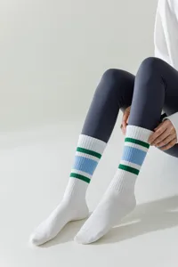 Detailed view of white athletic tube socks with blue and green stripes worn with grey leggings.