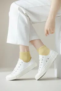 Nahaufnahme dünner Damen-Baumwoll-Netzsocken in Hellgelb kombiniert mit weißen Freizeitschuhen.