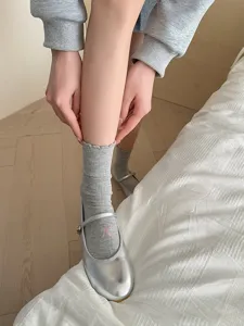 Gros plan de chaussettes en coton gris avec nœud rose brodé et joli bord à volants.