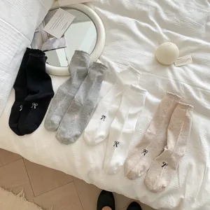 Gros plan sur des chaussettes mi-hautes en coton pour femmes avec broderie de nœud et volants.