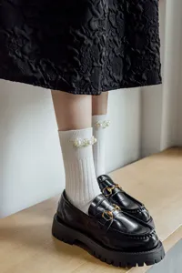Dettaglio di calzini bianchi a coste con eleganti perle sul polsino abbinati a mocassini neri.