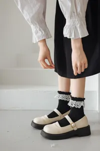 Gros plan de chaussettes Lolita noires avec bordure en dentelle blanche délicate et chaussures.