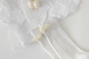 Primo piano dettagliato di calzini Lolita bianchi decorati con perle delicate sul bordo.